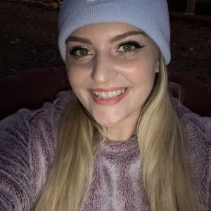 Person smiling, wearing a beanie, outdoors at night.